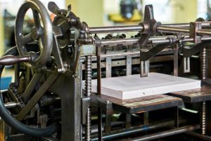 A close-up of an old printing press with paper, a lot of mechanisms, screws and wheels arranged in a structure. Modern invention at that point in history