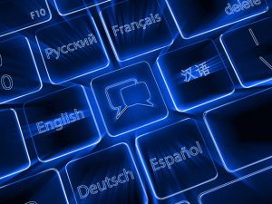 A zoomed in view of a modern keyboard shows black keys with different languages on each and the speech bubble symbol for translation in the middle, backlit in blue
